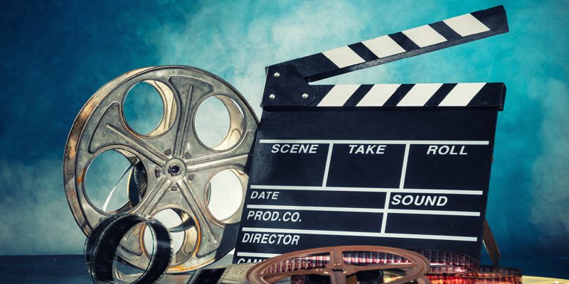 A Movie Clapboard And Movie Reel On Blue Background.